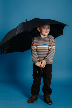 A little boy is standing under an open umbrella and smiling. On a blue backgroundの写真素材