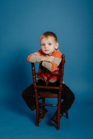A little boy in a cap sits on a chair and thinks. On a blue backgroundの写真素材