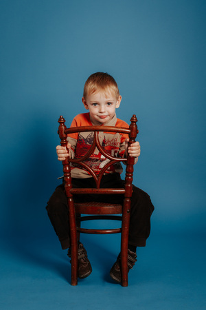 A little boy in a cap sits on a chair and smiles. On a blue backgroundの写真素材