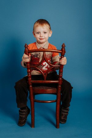 A little boy in a cap sits on a chair and smiles. On a blue backgroundの写真素材