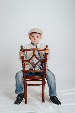 A little boy in a cap sits on a chair and smiles. On a white backgroundの写真素材
