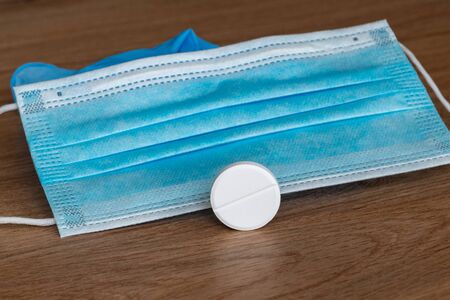 Coronavirus vaccine COVID-19. Rubber medical mask with a white tablet. Coronavirus tablet. Disposable items of protective equipment from coronavirus on a wooden background.の写真素材