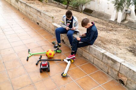 Mobile phone is a modern problem for children. Children play on the phone in the park. Toys and scooters are abandoned. Smartphone addiction in childrenの写真素材