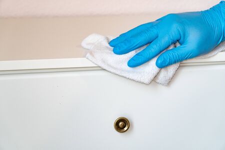 Protective blue gloves washes the furniture on the nightstand with a rag. Prevent the spread of coronavirus and infection COVID-19の写真素材
