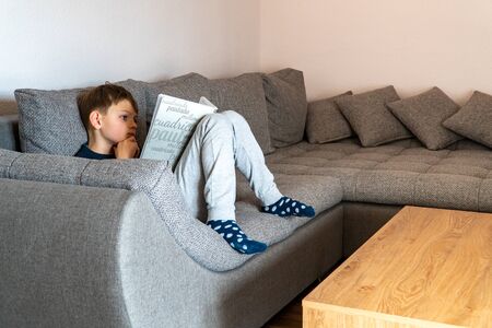 Isolated child is reading a quarantine book at home. Self-isolation, home quarantine. Distance education and quarantined training for the coronavirus epidemic. Distance learning at home.の写真素材