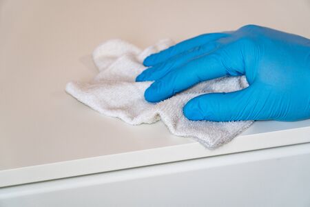 Protective blue gloves washes the furniture on the nightstand with a rag. Prevent the spread of coronavirus and infection COVID-19.の写真素材