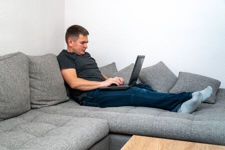 A quarantined coronavirus man is tired and lays on a sofa to work on the laptop. Self-isolation quarantine at home pandemic COVID19の写真素材