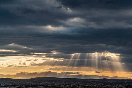 Panoramic view of dramatic sun ray through low clouds over city at sunset. The sun cuts through the clouds over the city. Sunbeams on the city.の写真素材