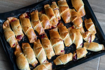 Pies with jam on a baking sheet. Cakes with jam on baking tray on wooden table. Homemade baking...