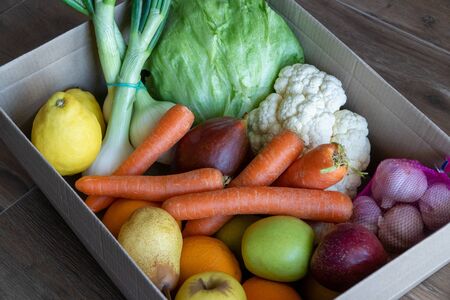 Vegetables in a cardboard box close-up. Fresh vegetables in cardboard box on brown wood background. Box for vegetarianism.の写真素材
