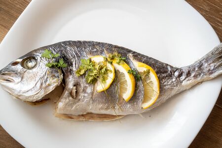 Homemade fried fish recipe. Dorada fish fried with lemon and parsley on a white plate.