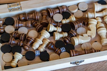 Checkers and chess are randomly mixed scattered in a wooden box. Close up viewv