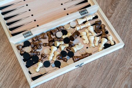 Checkers and chess are randomly mixed scattered in a wooden box.
