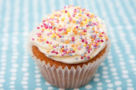 A freshly made homemade cupcake with round sprinkles on a pale blue napkin with white spots.  Differential focus on the cupcake.の写真素材