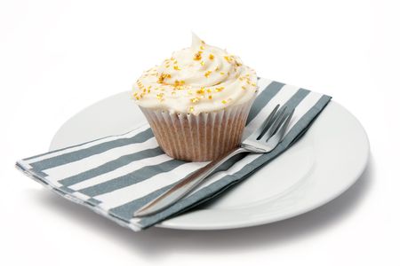 A freshly made homemade cupcake with gold stars sits on a plate with a stripy napkin and a dessert fork.  Isolated on white.の写真素材