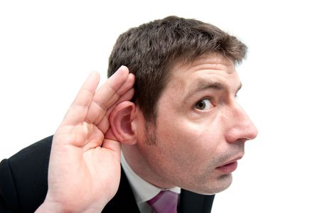 A mid thirties businessman in a black suit leans towards the camera showing that he is listening for something.の写真素材