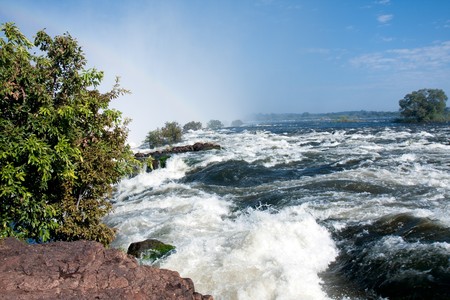 The raging torrent of the mighty Zambezi river in full flood at the very edge of the Victoria Falls.  The spray cloud creates a subtle rainbow.の写真素材