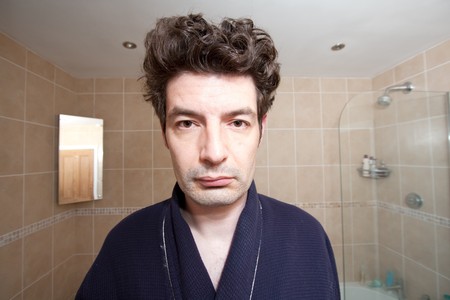 A man ho has just woken up looks into the bathroom mirror.の写真素材