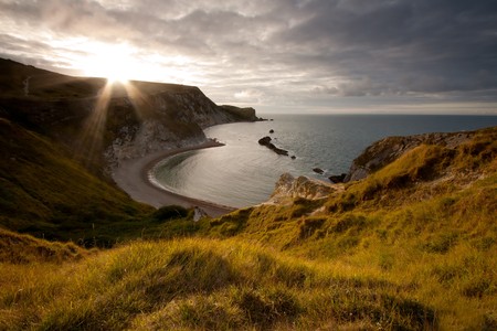 The sun peeps out over the cliff top over looking Man-O-War Cove on the Jurassic Coast in Dorset, UK.の写真素材