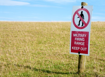 A scratched and worn red and white keep out sign on a wooden post in a field of green grass with blue sky.  Focus on the sign.の写真素材