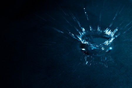 A blue coloured splash of water on a dark background.  The water is very shallow and you can see the reflection of the splash.の写真素材