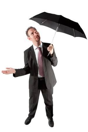 A full length of a mid thirties business man.  The man is standing underneath a black umbrella and checking if it raining.  Studio isolated on a white background.の写真素材