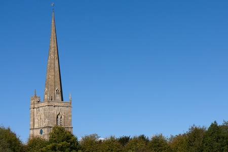 A background or border image of the top half of an English church steeple.  Clear blue sky as copyspace and the tops of trees on the bottom.の写真素材