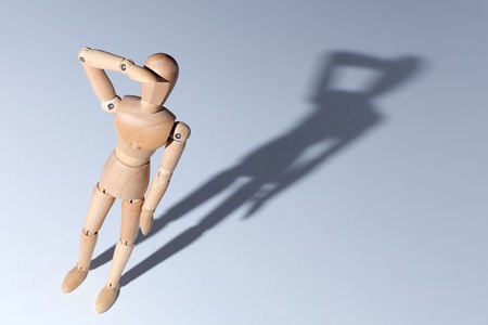 A wooden mannequin on a blank background casting an obvious shadow.

The pose is one of saluting, searching or shading the eyes.の写真素材