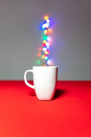 White cup standing on the red background with bokeh steam coming from it. New Year, Christmas and holidays celebrationsの写真素材