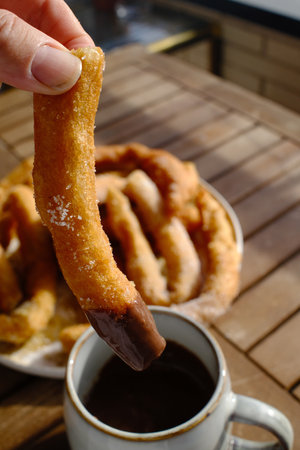 Cup of coffee and churros on wooden table, closeup