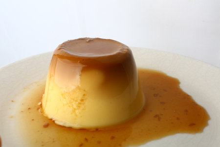Close up of a caramel custard pudding on a white plate.