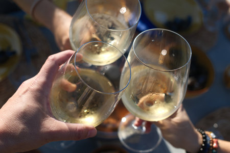 Close-up of two hands toasting with white wine at an outdoor party