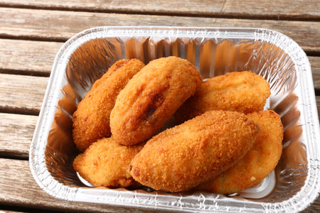 Tasty chicken nuggets in foil box on wooden table, closeupの写真素材