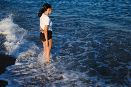Young woman standing on the beach and looking at the sea. Black sand.の写真素材