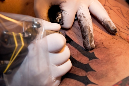 a tattoo artist imprinting his art with black ink on a stomach of a young guyの写真素材
