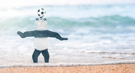 miniature circus bamboo panda teddy bear stands on beach Gulf of Siam to his ankles in water. and chasing ball on nose. soccer player juggling beautiful background blur on the beachの写真素材