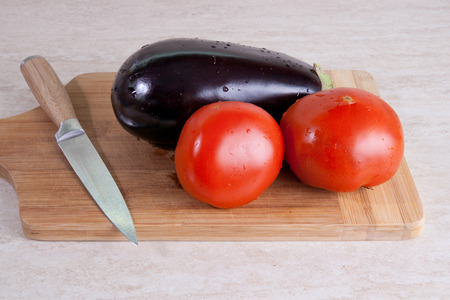 Eggplant and two tomatos on a cutting boardの写真素材