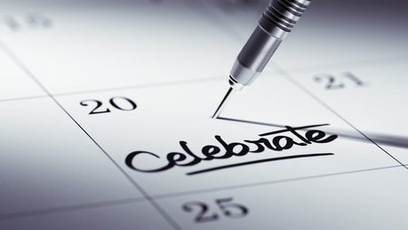 Concept image of a Calendar with a golden dart stick. The words Celebrate written on a white notebook to remind you an important appointment.の写真素材