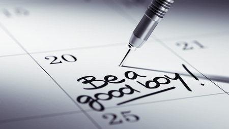Concept image of a Calendar with a golden dart stick. The words Be a good boy written on a white notebook to remind you an important appointment.の写真素材