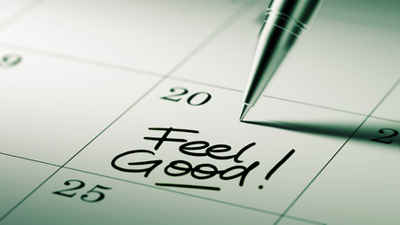 Closeup of a personal agenda setting an important date written with pen. The words Feel Good written on a white notebook to remind you an important appointment.の写真素材