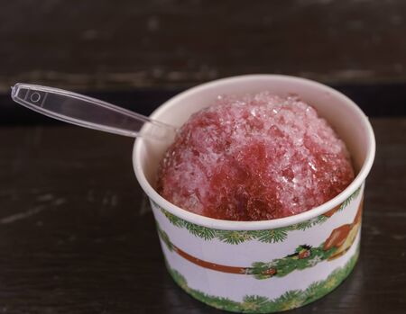 shaved ice with strawberry syrup in small bowl on wooden table.の写真素材