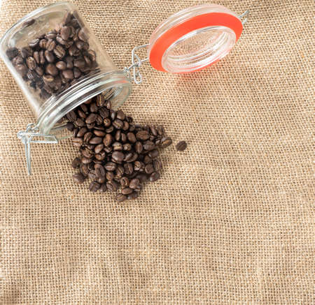 glass bottle with coffee beans fall down spread out on a sackcloth from top view.の写真素材