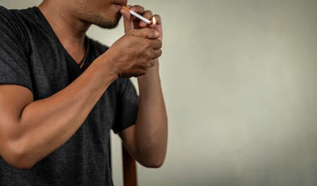 asian guy lighting a cigarette behind the wall. concept for narcotic, illness.の写真素材