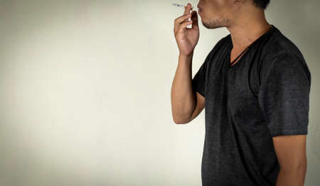 Asian guy holds  a burning cigarette for smoking behind the wall. concept for narcotic, illness, crime.の写真素材