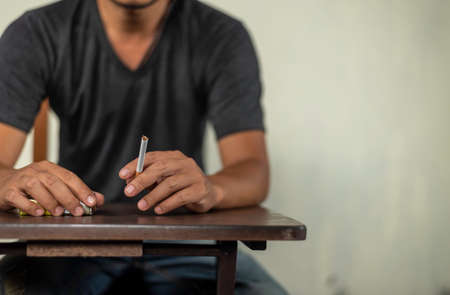 man sit in the table and holds cigarette for smoking. concept for cancer, illness, crime.の写真素材