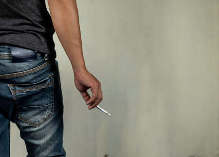 man holds a burning cigarette look from back. concept for crime, illness, cancer, narcotic.の写真素材