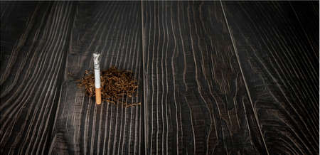 a burning cigarette with pile of tobacco on a wooden backgroundの写真素材