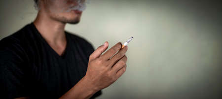 man holds cigarette behind the wall during smoking. illness concept.の写真素材