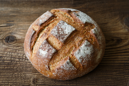 A freshly baked rustic, loaf of bread on an old wooden table