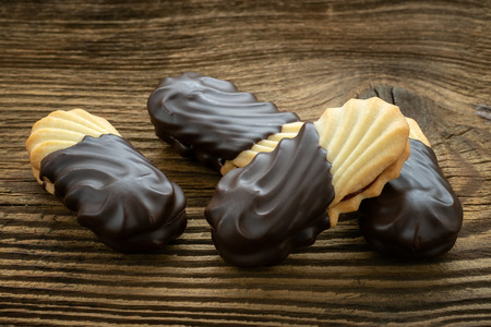 Cookies on wooden table. Biscuits with filling on wooden desk. Sweet cookies dipped in chocolate.の写真素材